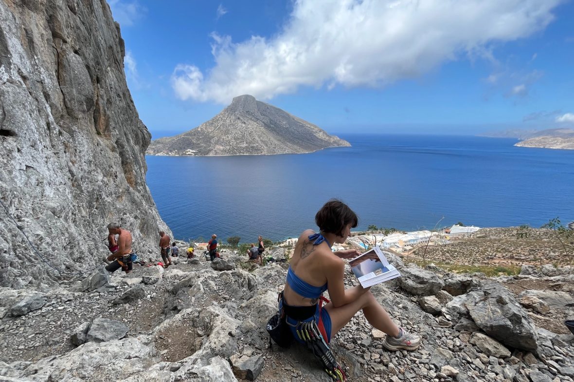 A climbing woman sits at the crag reading guidebook