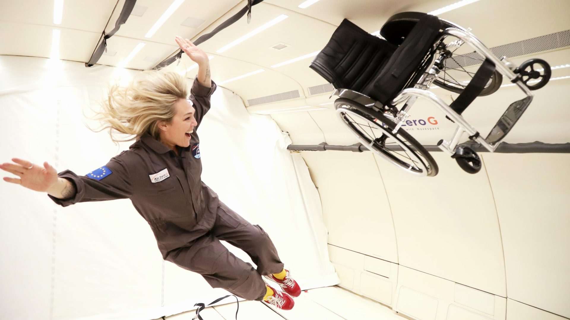 A woman and hert wheelchair are elevated from the ground in a zero gravity room.