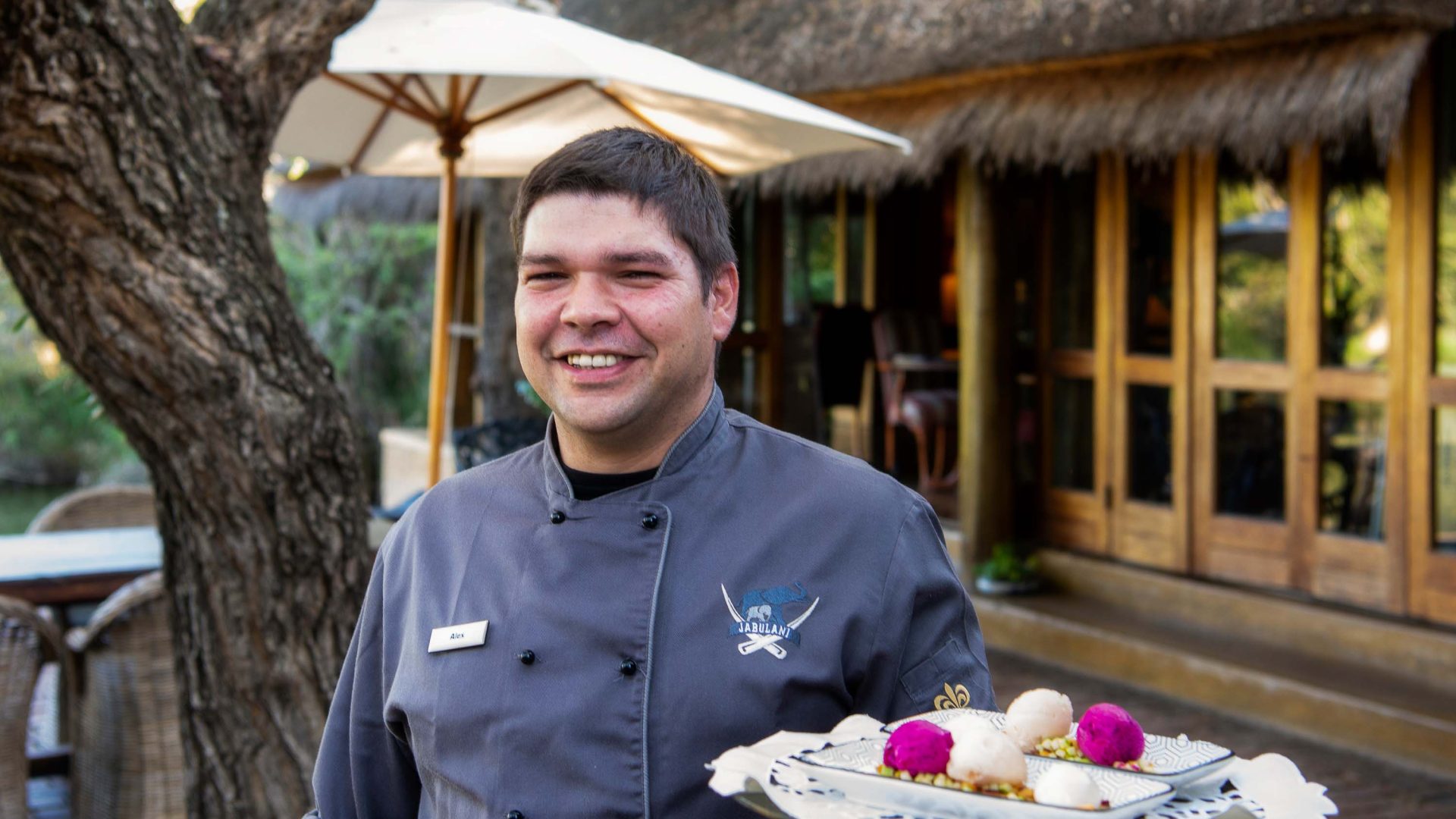 A smiling chef holds a plate of food.