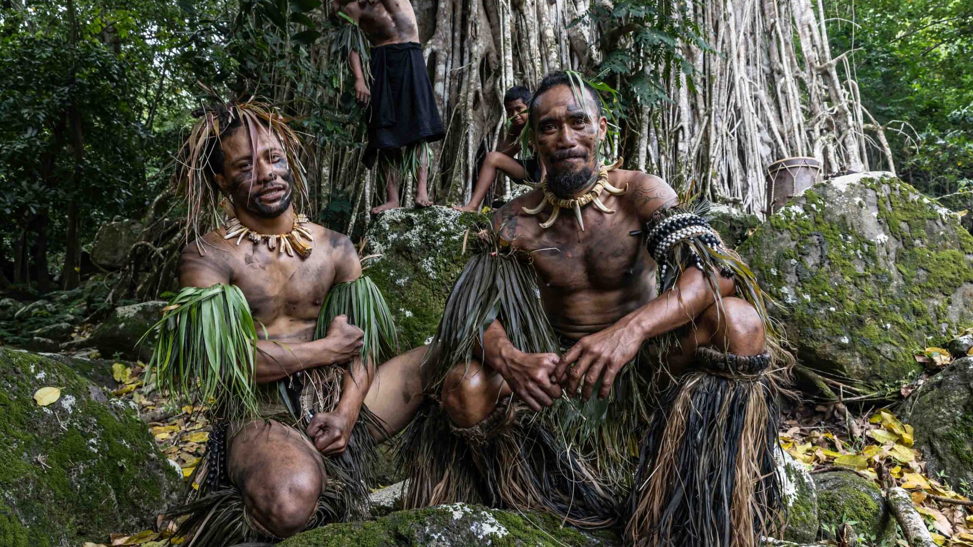 Men in traditional clothing and tattoos pose for a photo in amongst the trees.