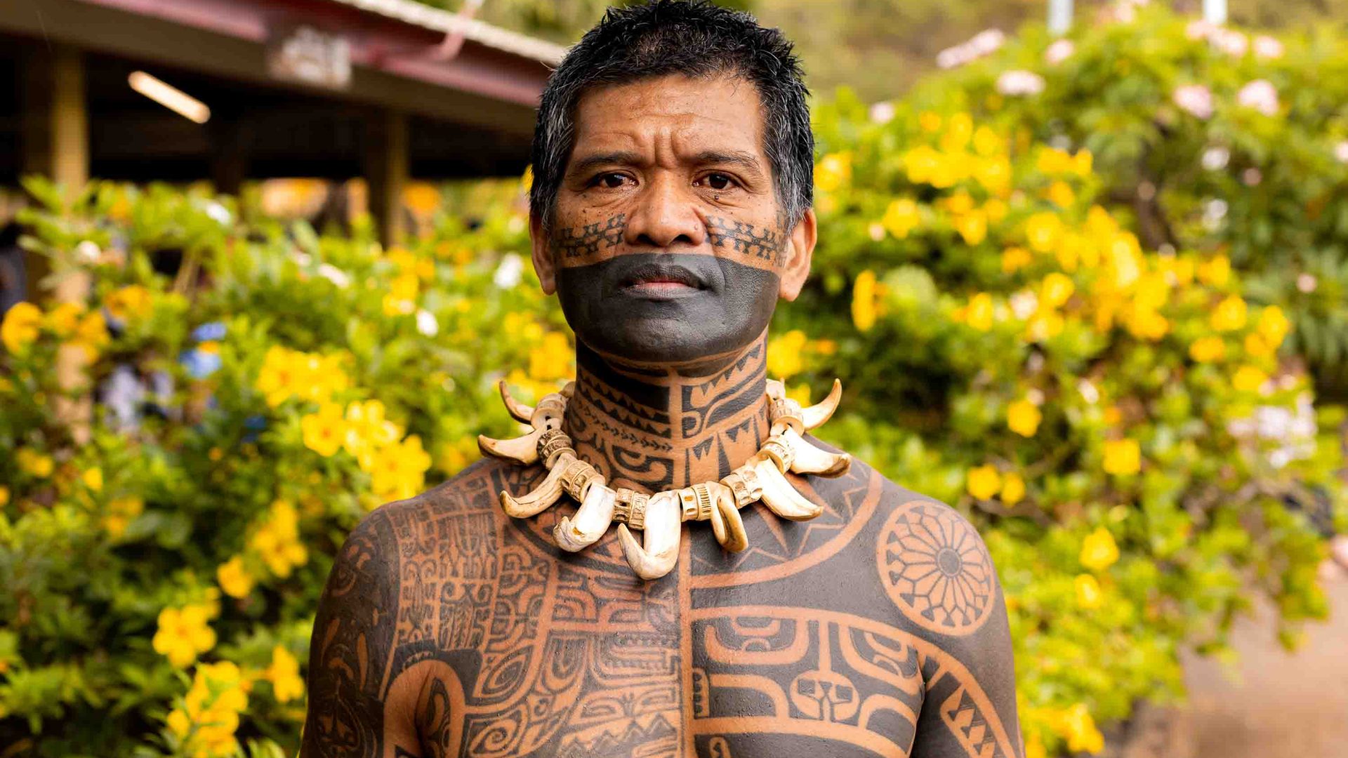 A man with lots of tattoos wears bone carvings as a necklace.