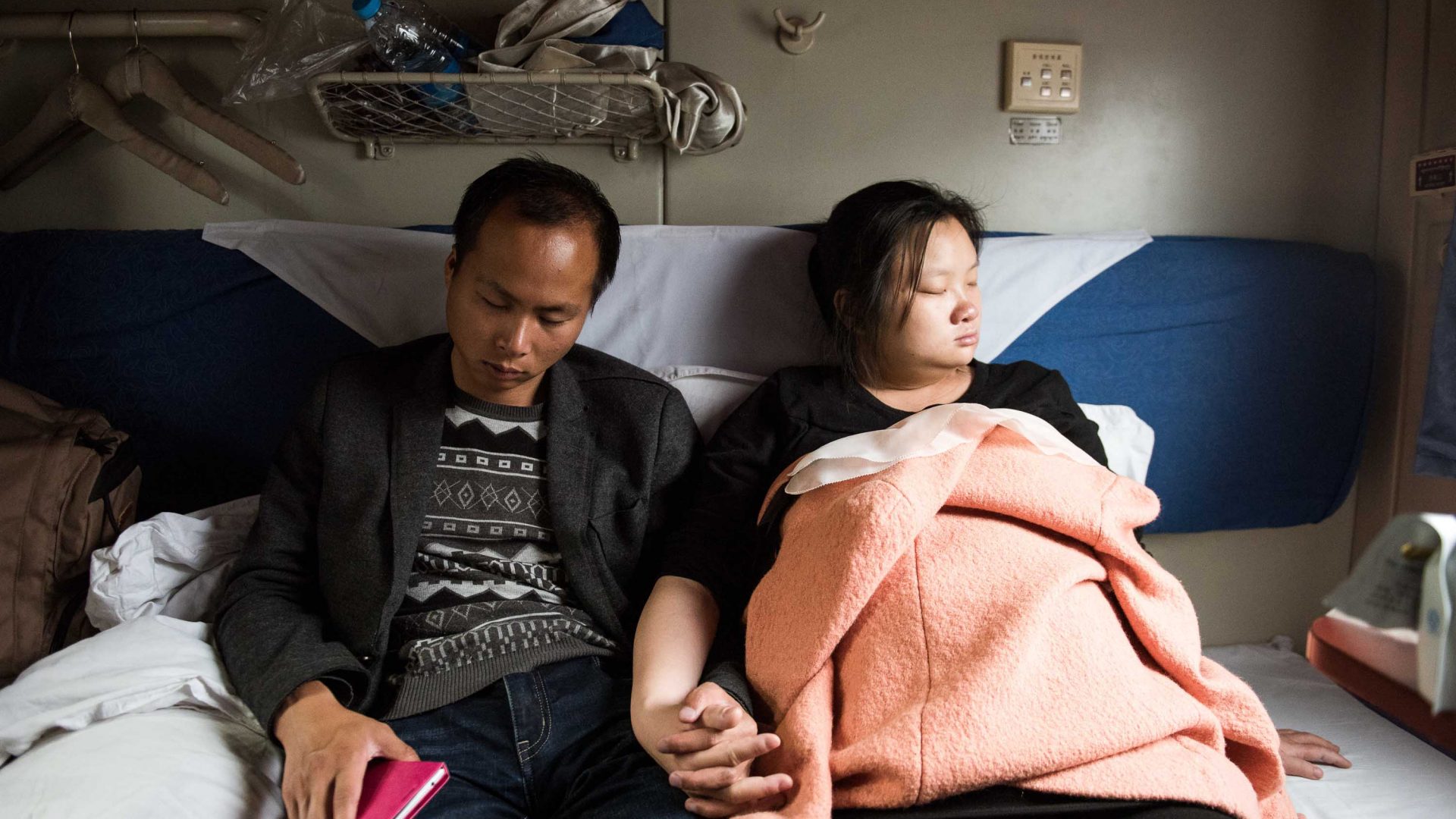 A couple sleep hand-in-hand during a train journey.