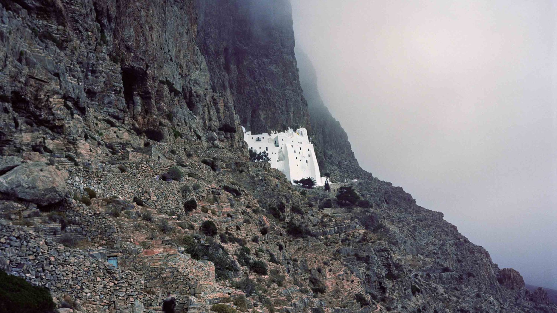 A white building stands in stark contrast to the dark cliff face around it.