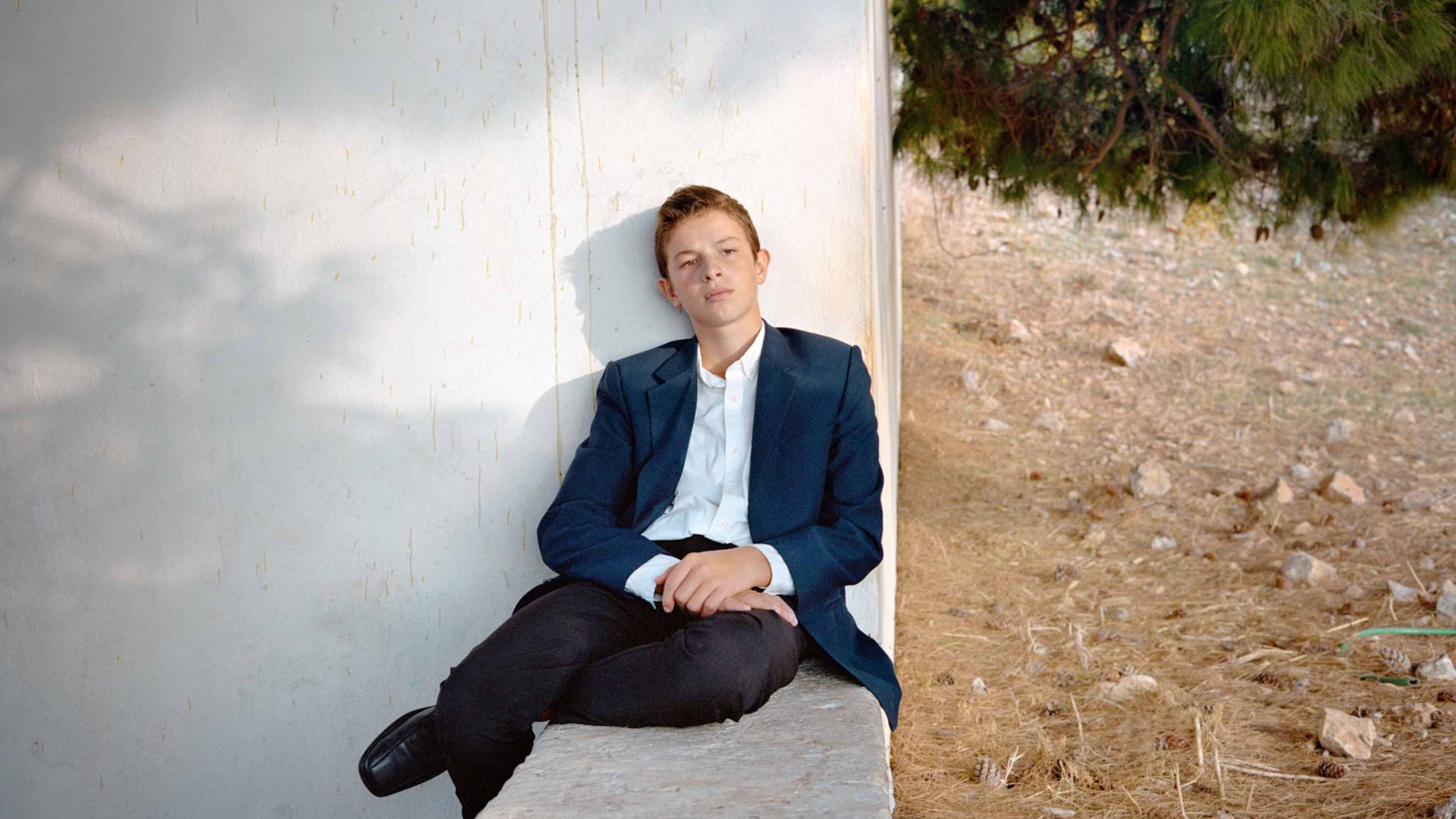 A young man looks forlorn as he sits on a wall looking away.