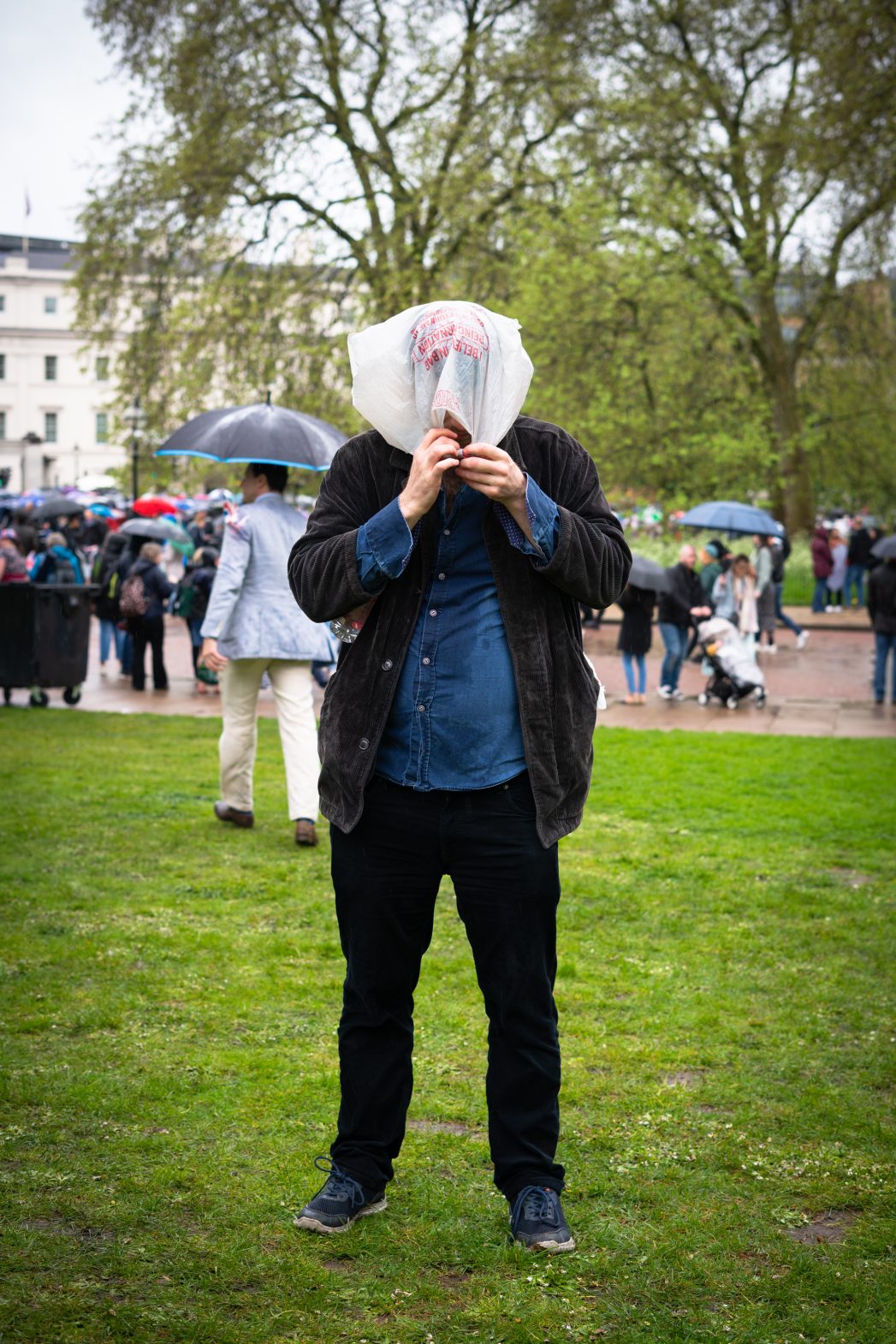 A man in the park covers his face from the rain.