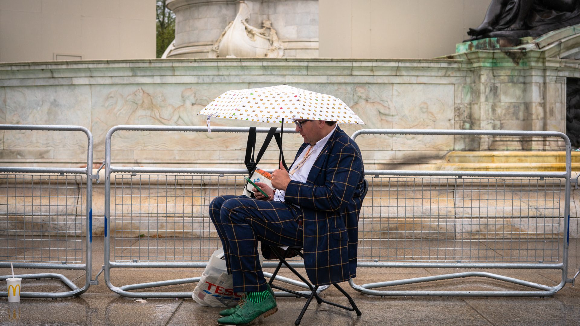 A man in a suit sat on a chair beside a crowd control barrier.