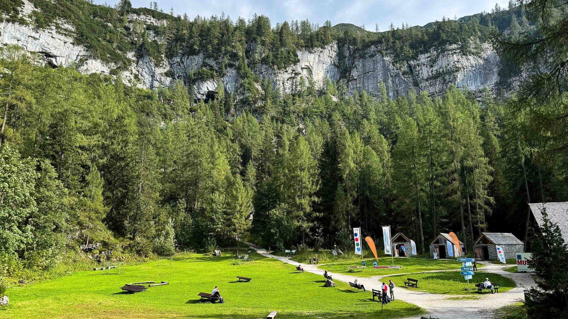 A Nature Park surrounded by mountains, has stalls with visitors walking round.