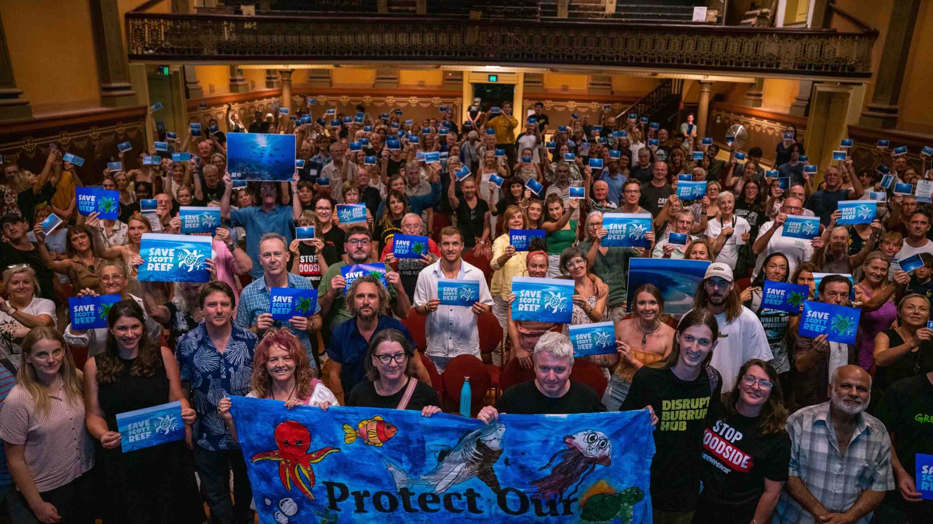 300 people stand together and hold signs advocating for Scott Reef.