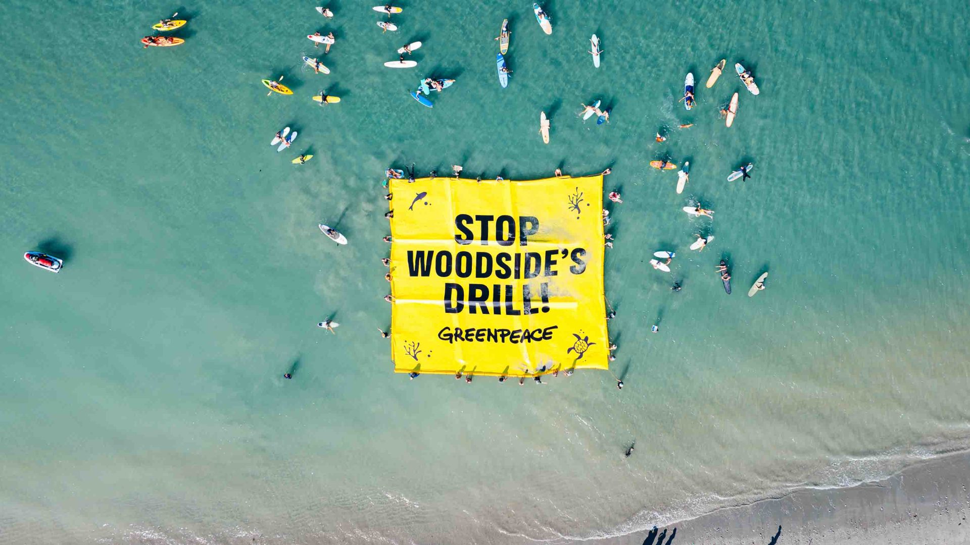 An aerial photo of people on kayaks surrounding a sign that reads 'Stop Woodside's drill'.