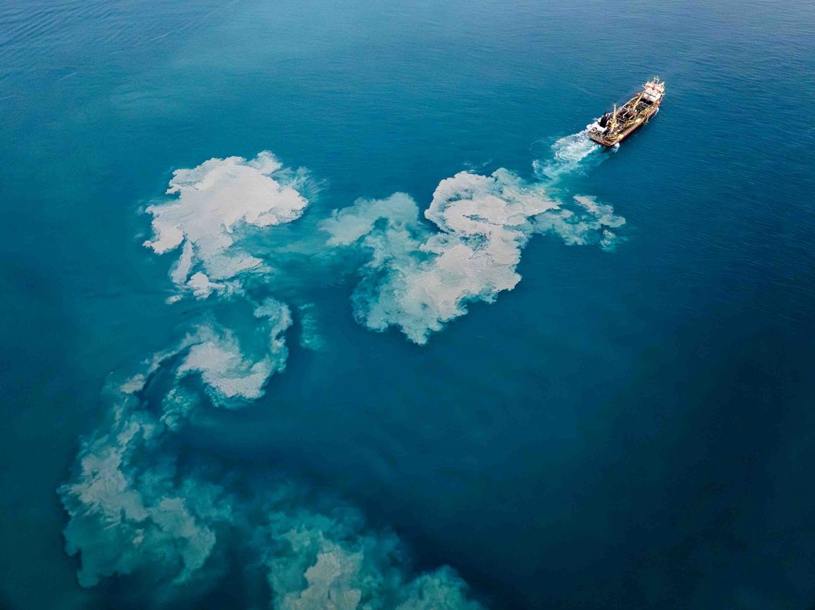 A boat that is dredging leaves clouds of sea bed in its wake.