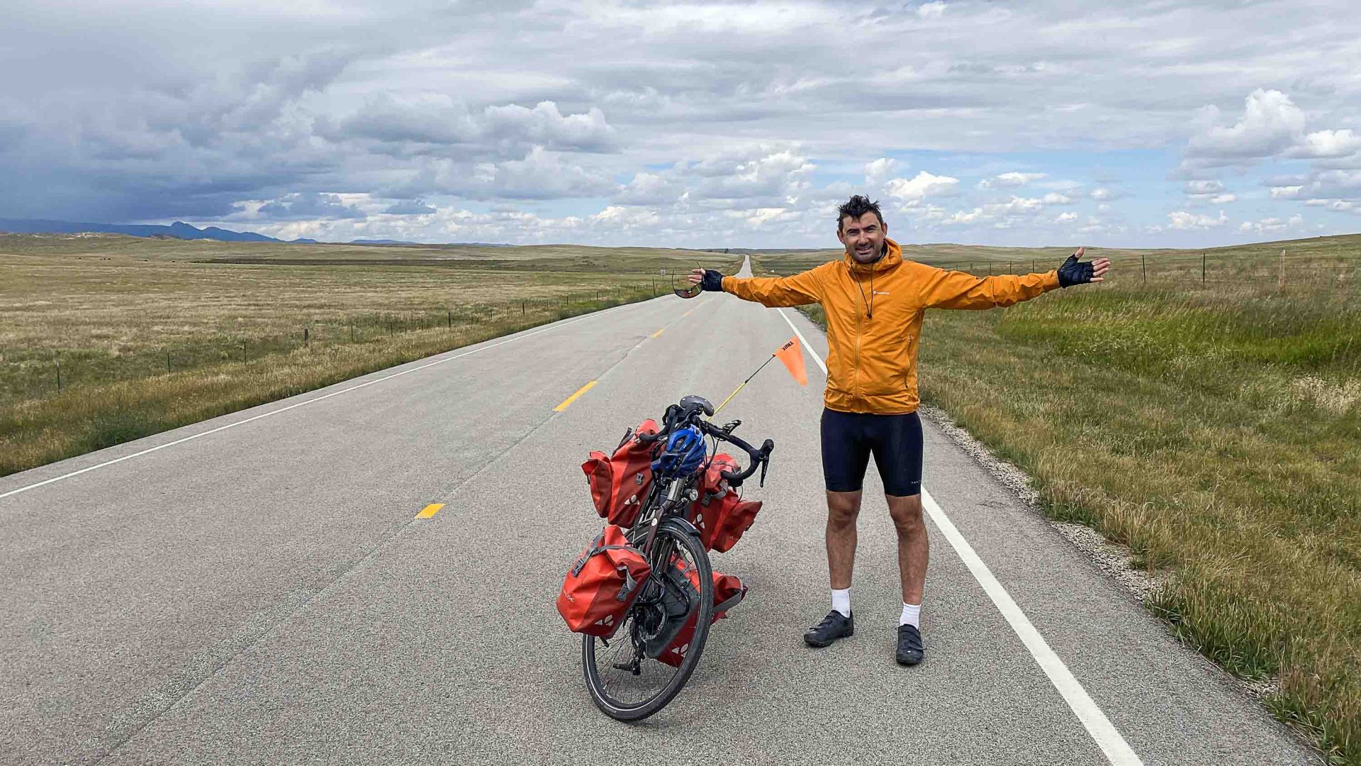 Simon with his bike on the road. Vast plains stretch to either side of him.