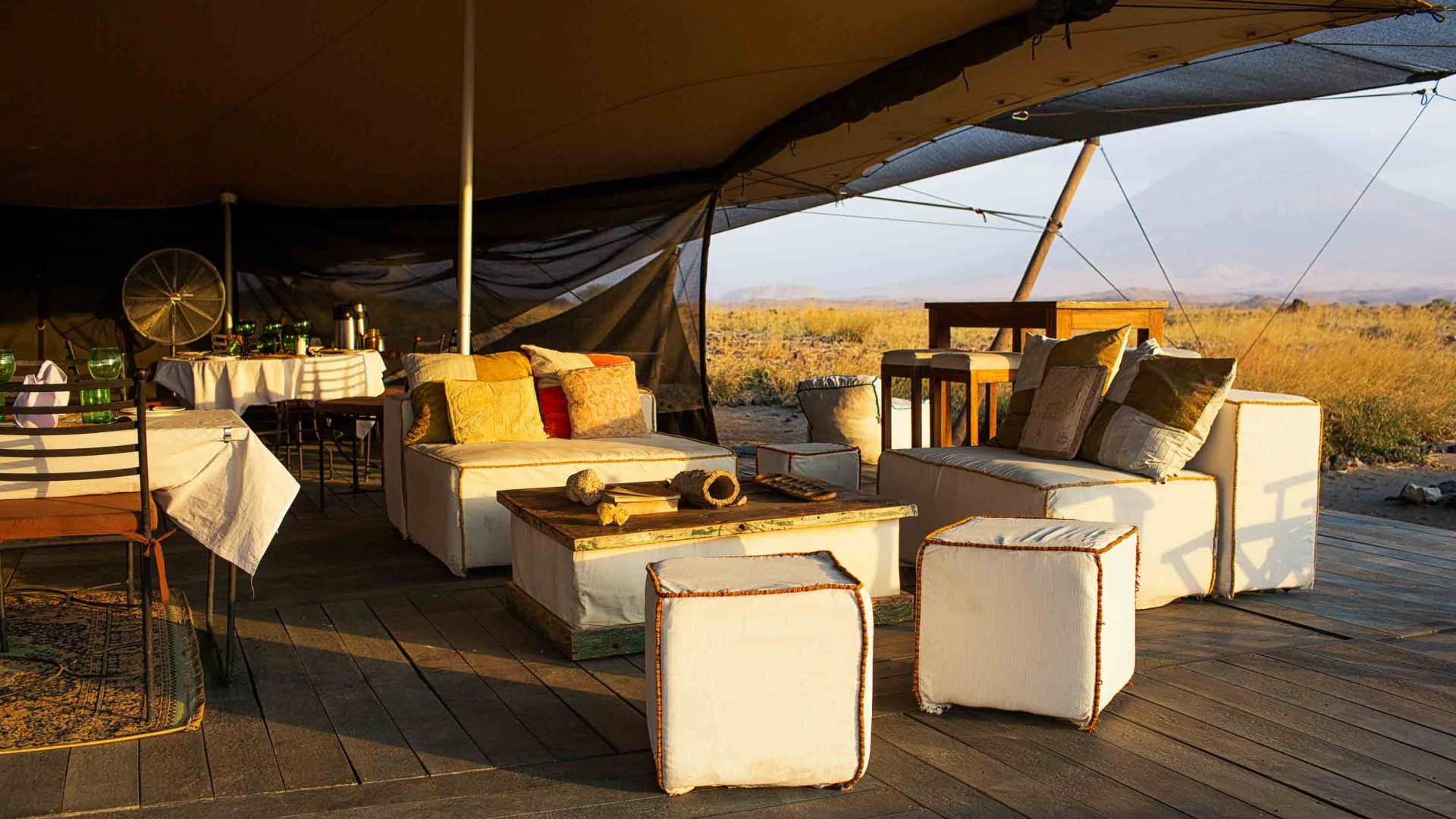 Tables and chairs in an outdoors camp area, under a canvas roof.