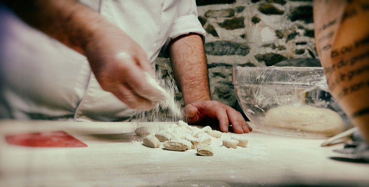 Hands sprinkle flour over some white dough.