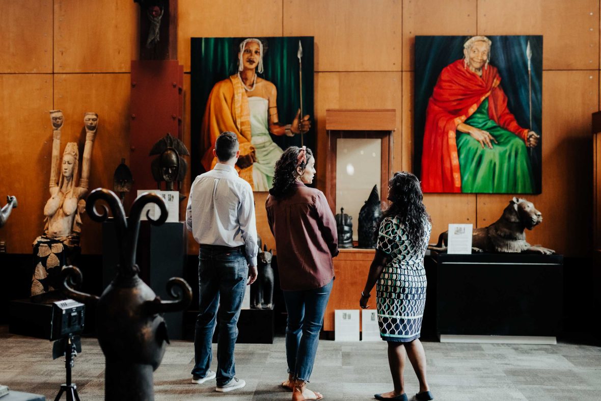 Three people have their backs turned as they look at art on a wall.