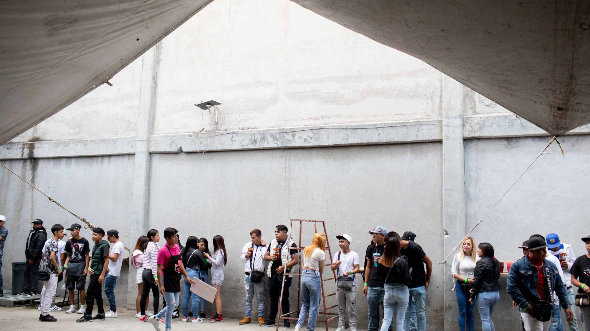 A group of people stand against a concrete wall drinking micheladas at Dolls Drinks.