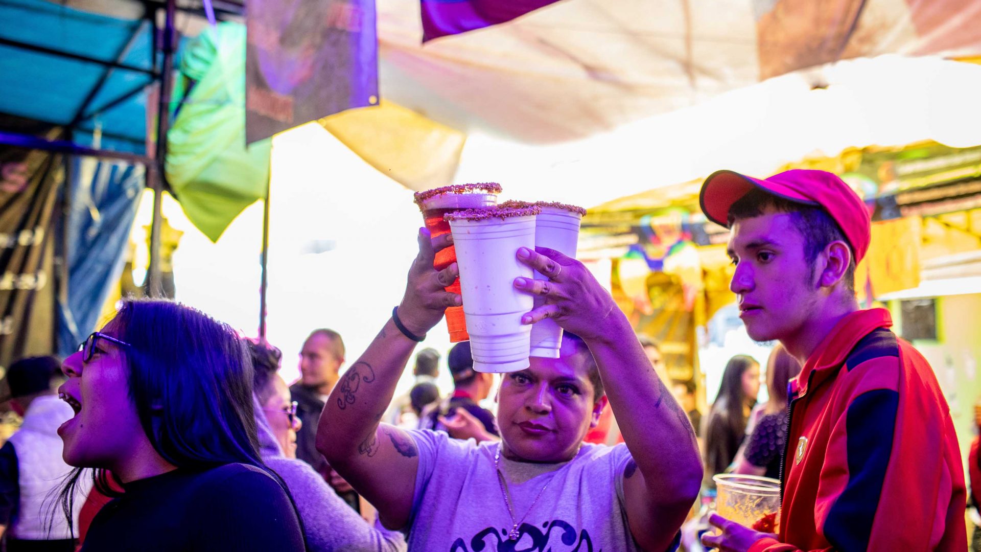 A man carries micheladas through a crowd of people.