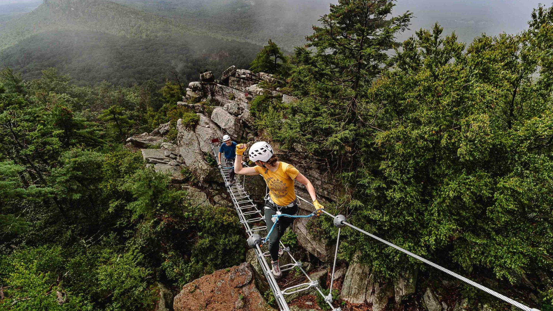 Two people ascend a via ferrata, making positive hand signals to each other.