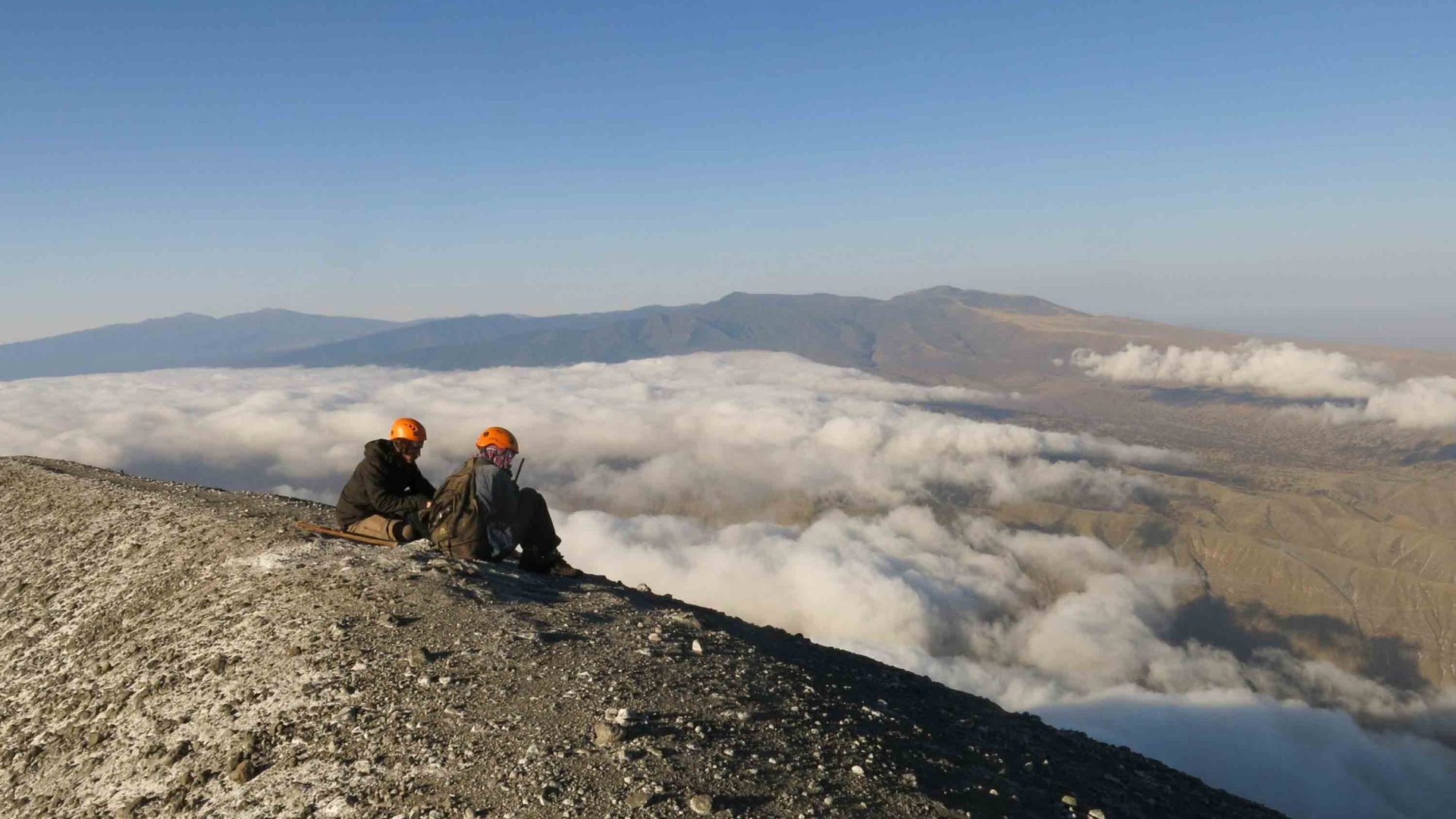 Two people look down over the clouds from the top of the volcano.