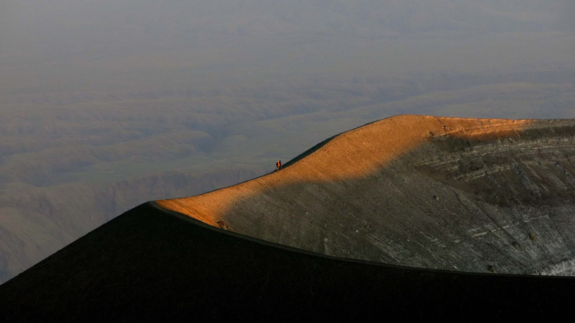 Two figures can be seen walking along the rim of the volcano.