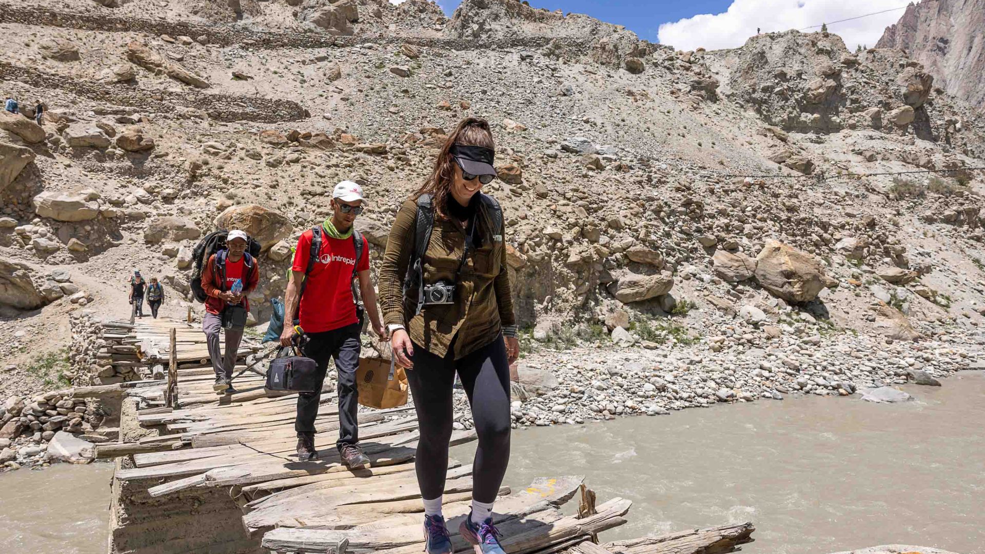 Trekkers and Intrepid guides cross a river using a small bridge.