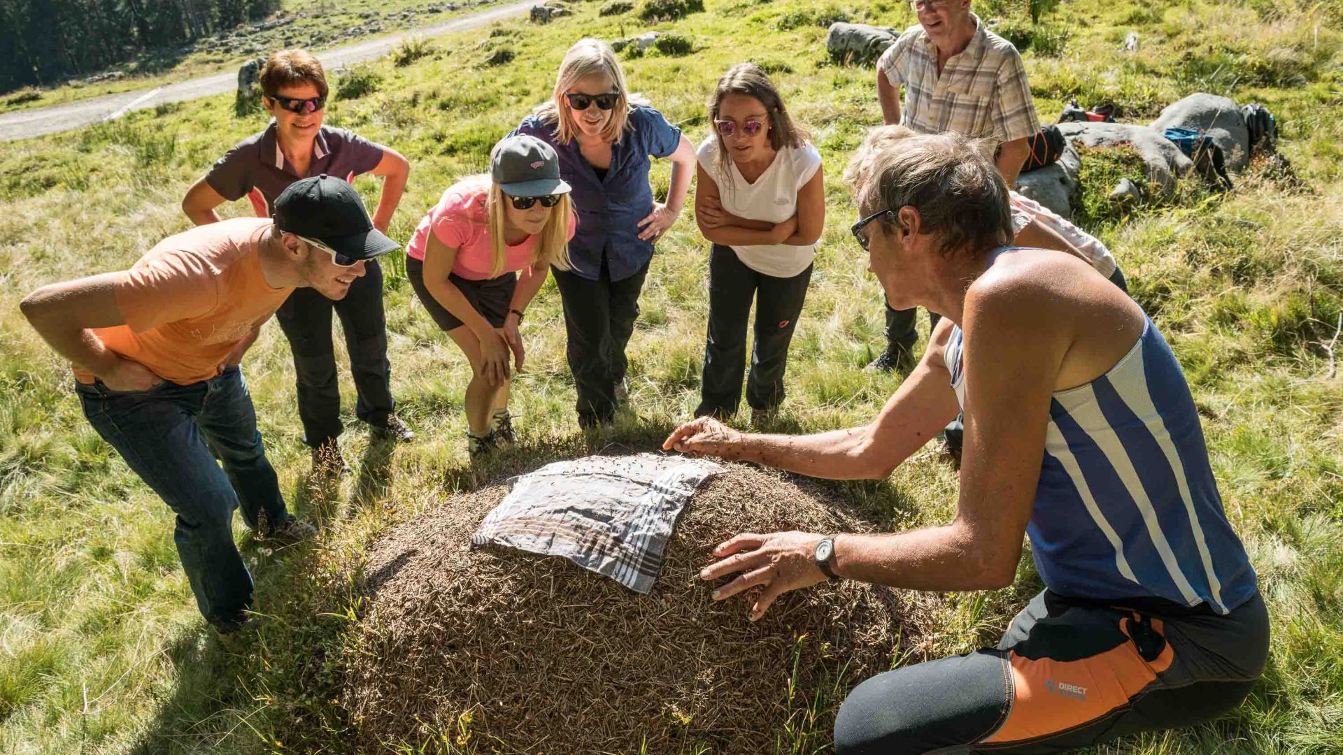 A man leans down and shows a cloth over a mound of earth to a group of people.