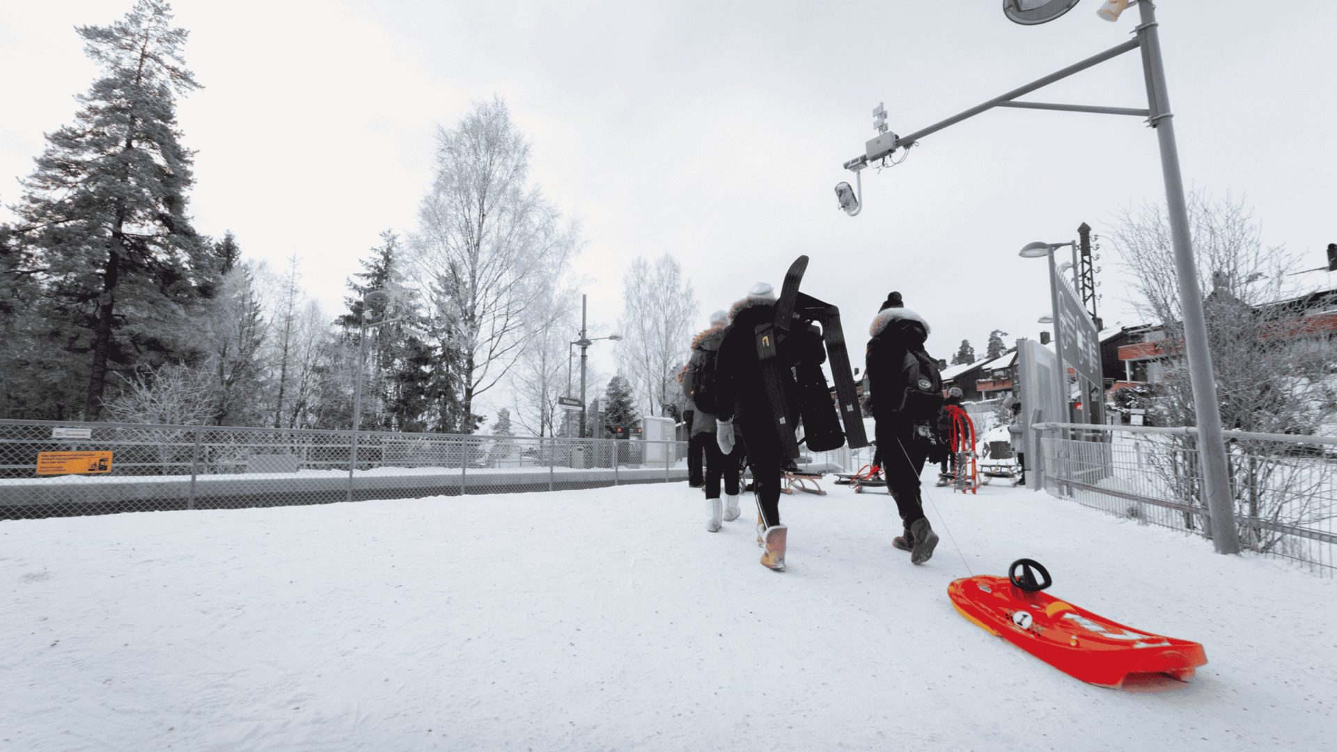 On a snowy day, people drag a red sled toward a metro platform.