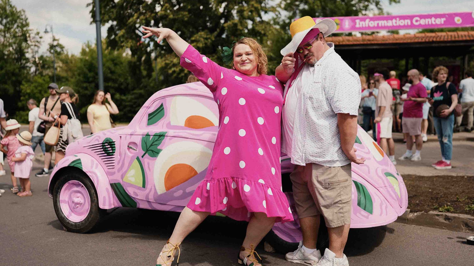 Two people pose in front of a pink Volkswagen painted with soup ingredients.