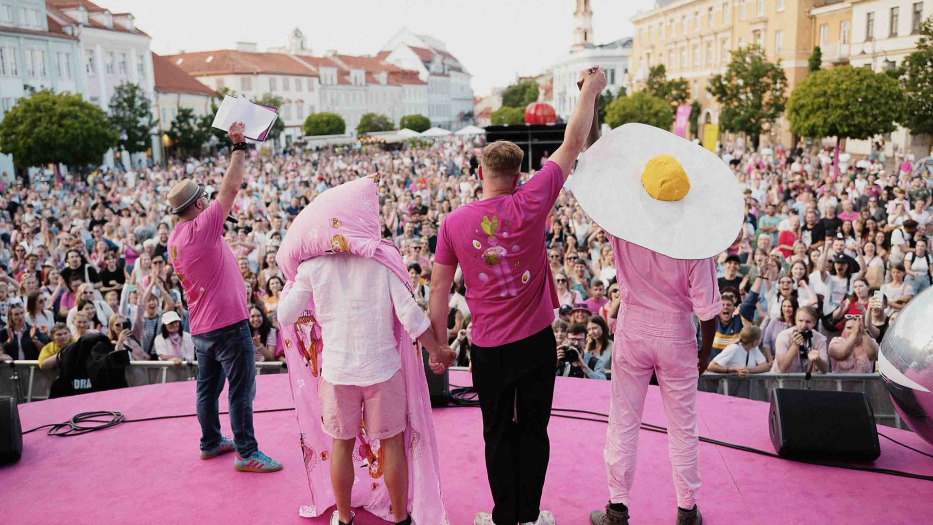 People dressed in costume wave out to a crowd of spectators from a stage.