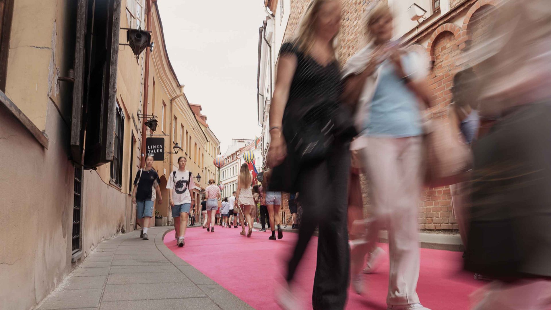 People walk down the length of a street covered in pink carpet.