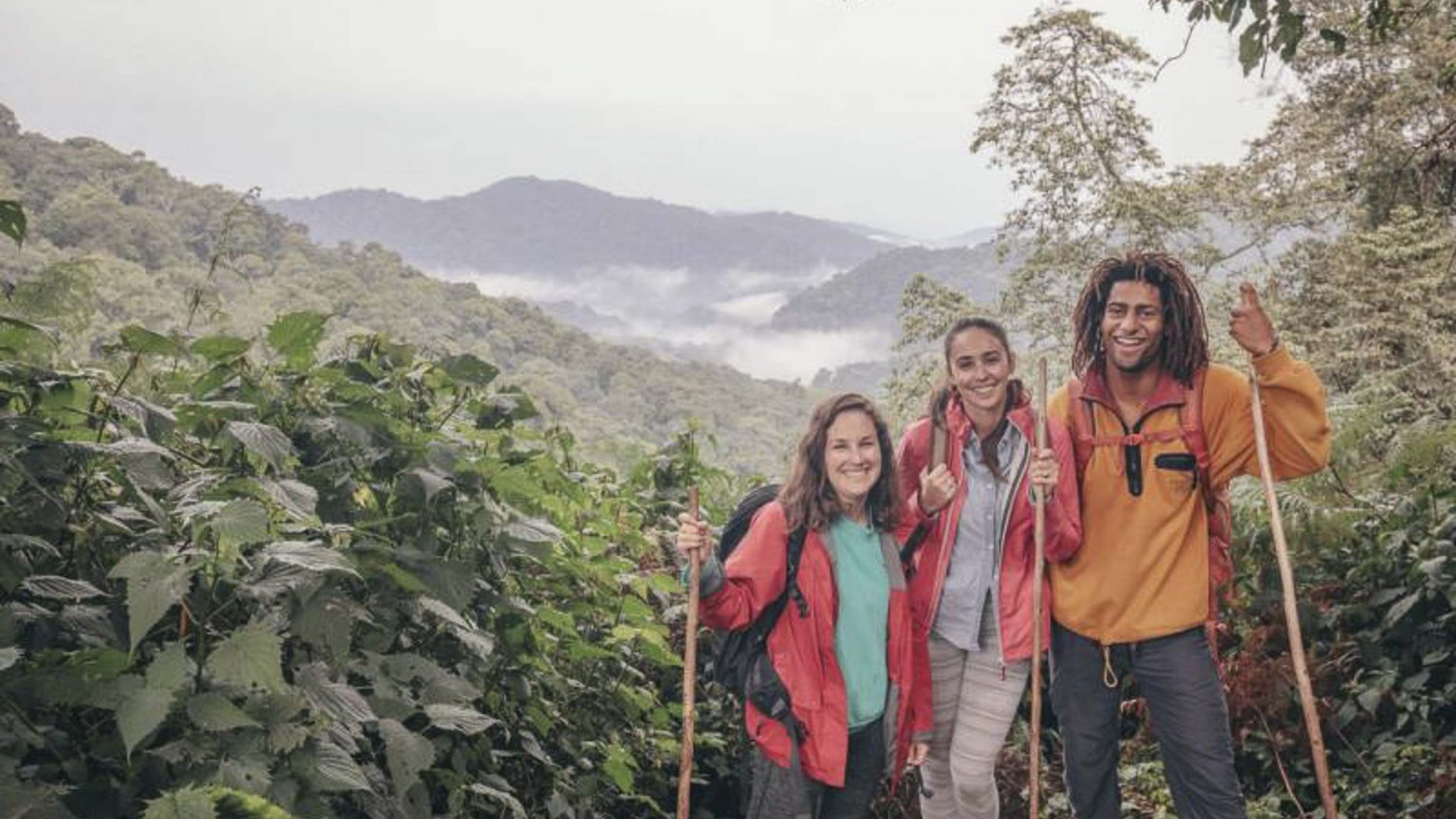 Three people smile to camera during a gorilla trek in Uganda.