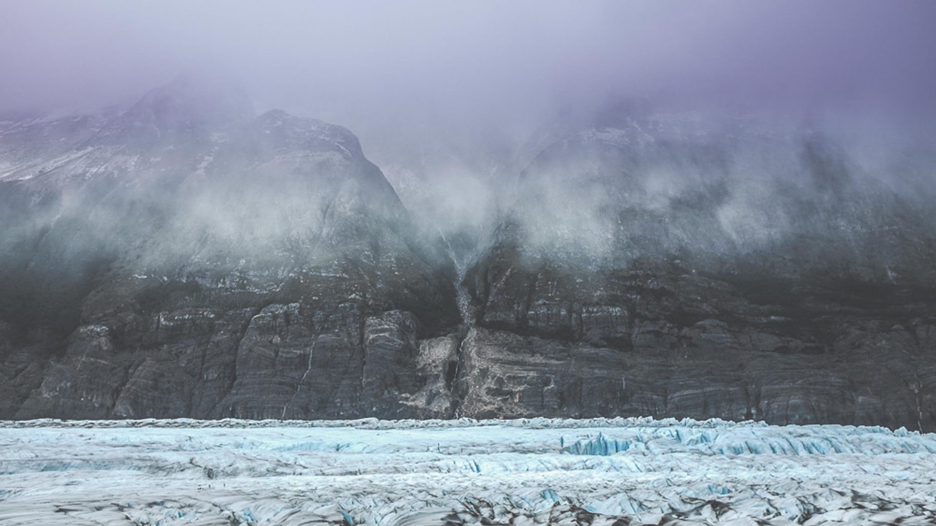 Turquoise water and snow capped mountains shrouded in clouds in Patagonia.