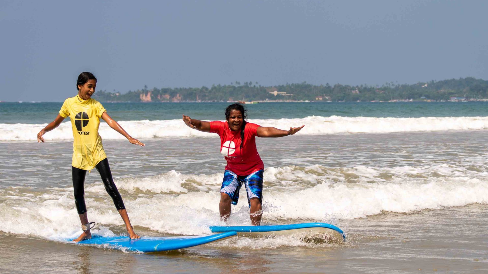 Two women surf on small waves.