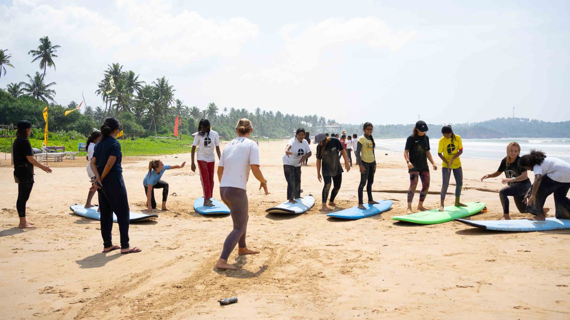 A person gives surf lessons to people on the sand with boards in front of them.