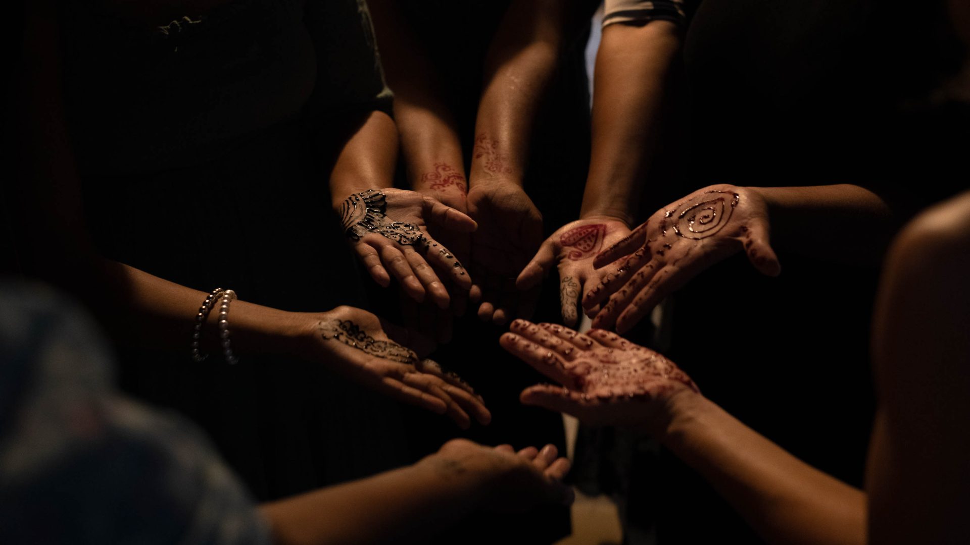 Hands painted with henna are held out in a circle.