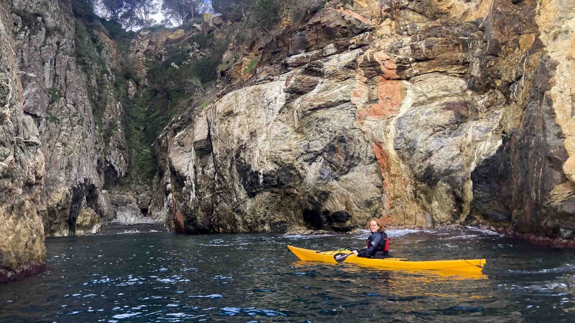 A woman on a yellow kayak near some rocks.