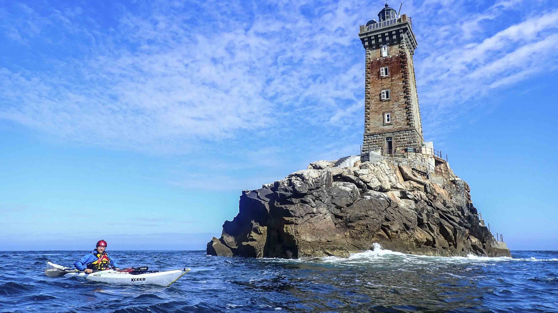 A man kayaks toward a lighthouse.