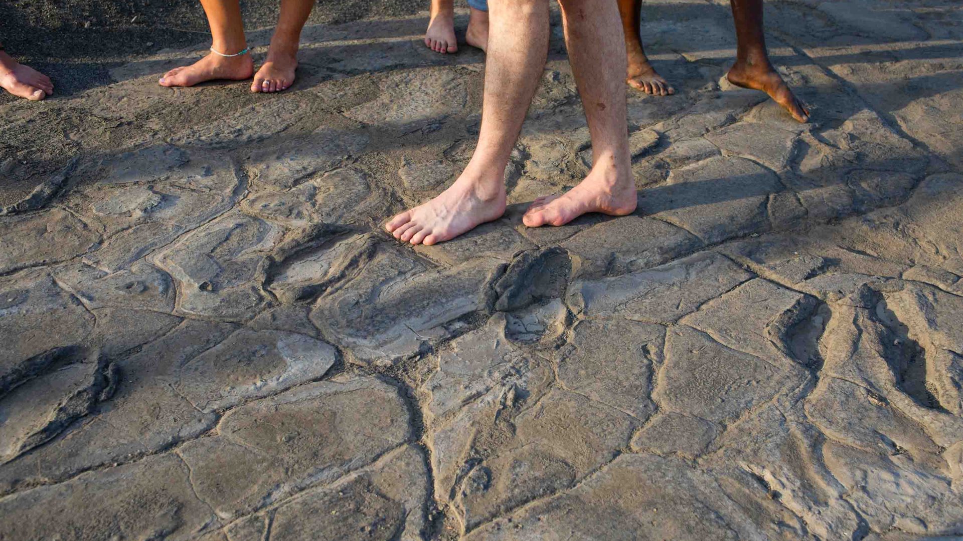 People stand alongside some fossilized human footprints near lake Natron.