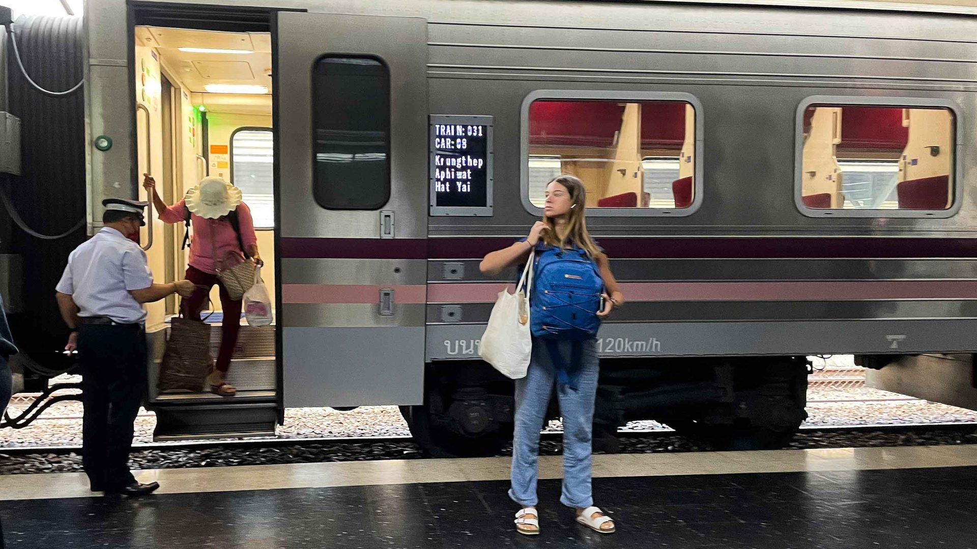 A woman stands in front of a train on the platform while someone else disembarks on the stairs.