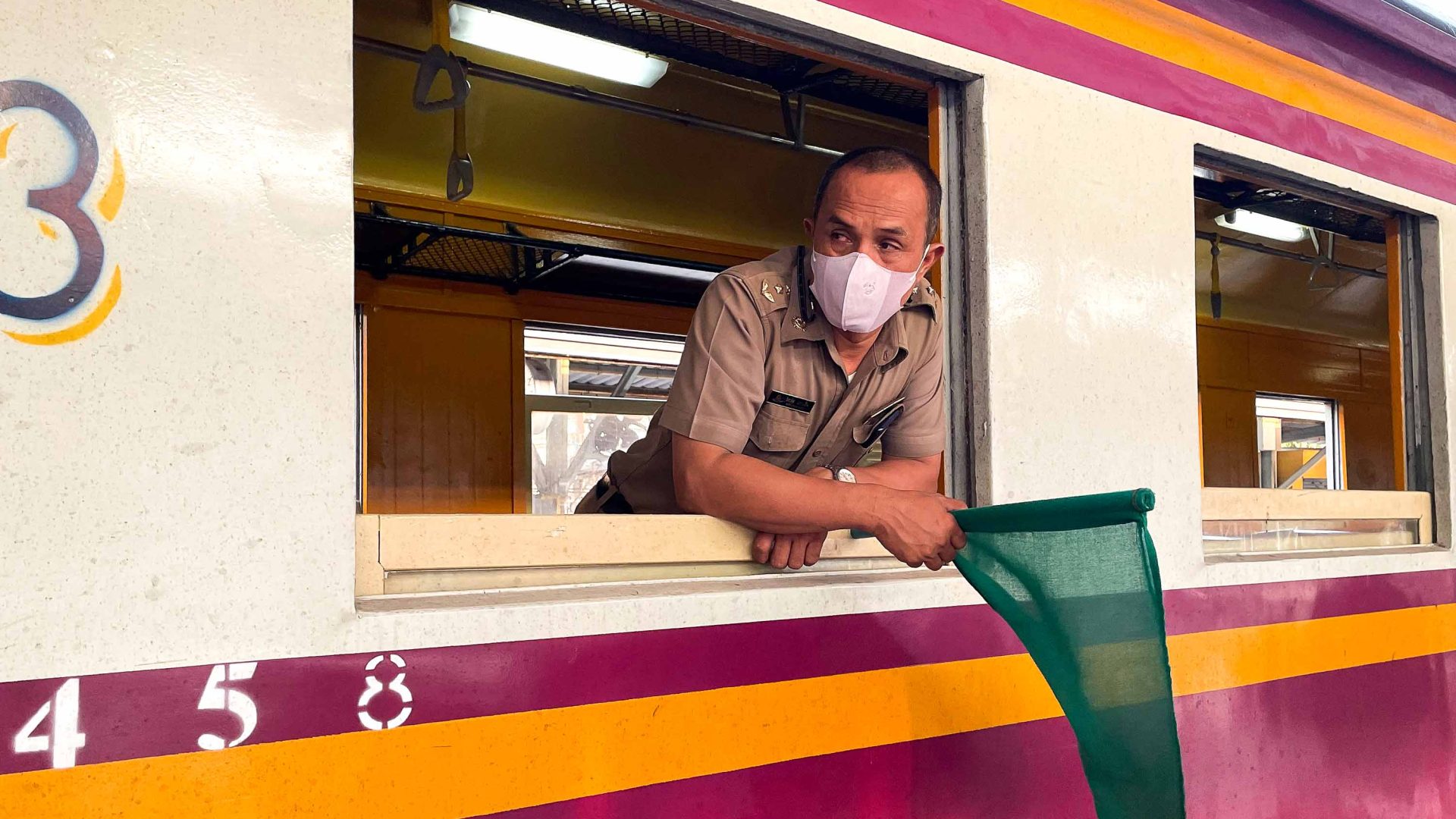 A train guard leans out the window of a train.