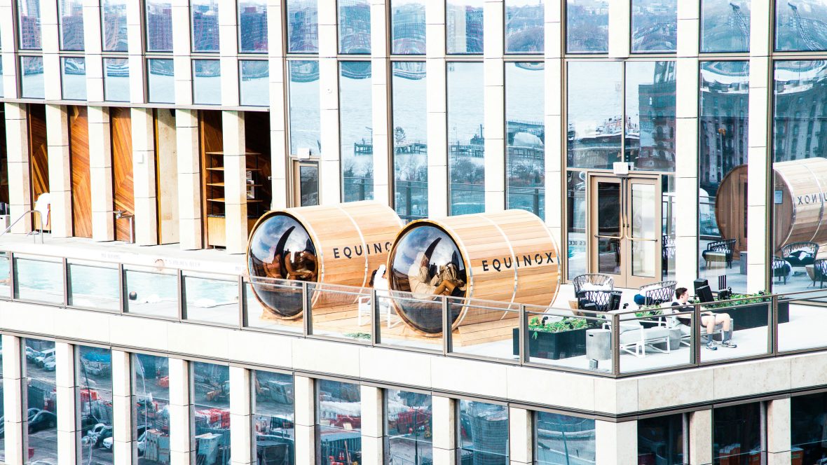 People sit inside barrel saunas on the balcony of a hotel.