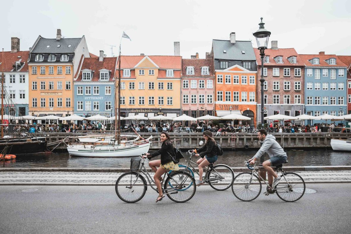 Tourists ride bikes along the promenade which is lined by colorful buildings and patios of restaurants.