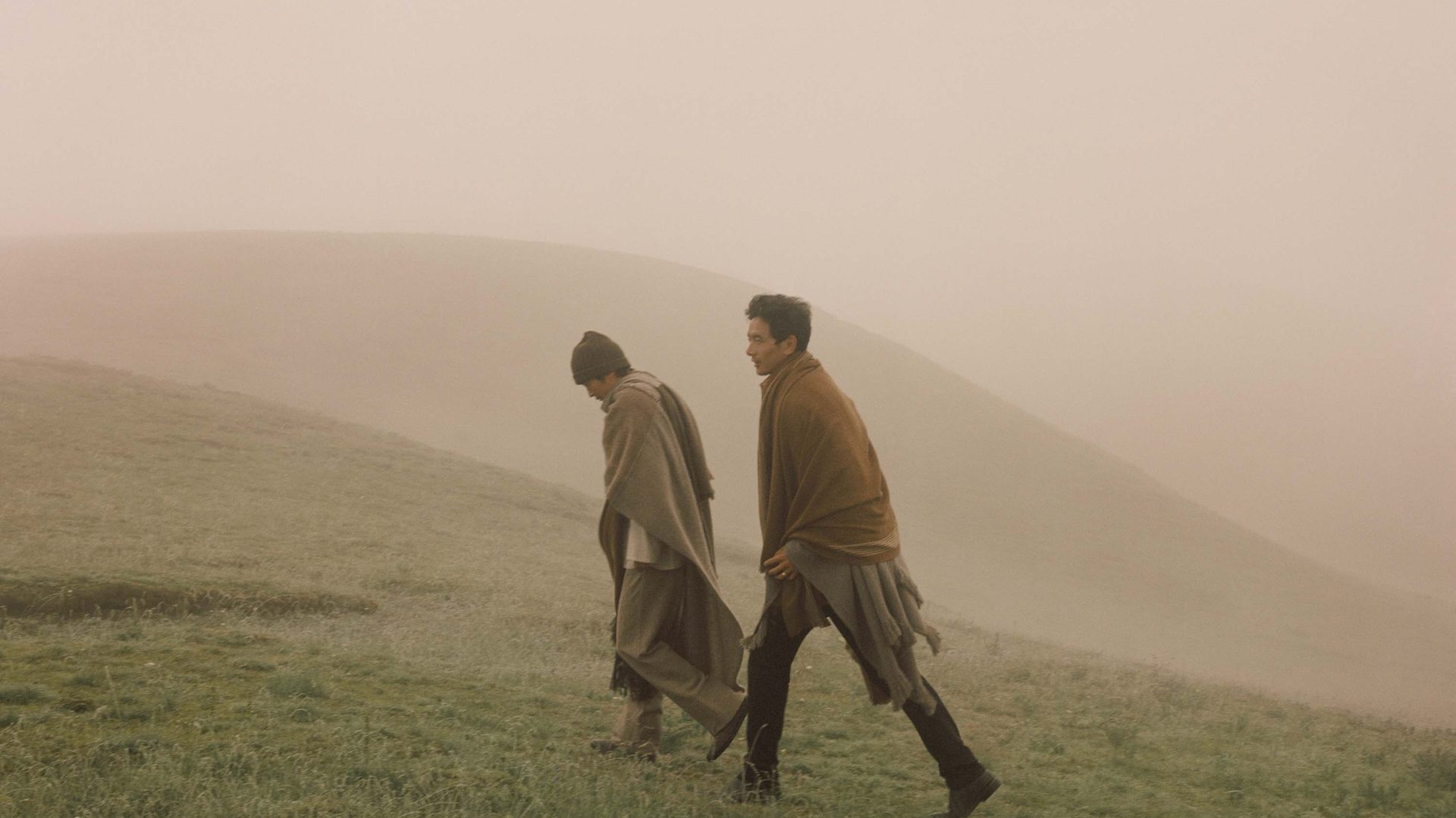 Two men walk up a hill through soft orange light.