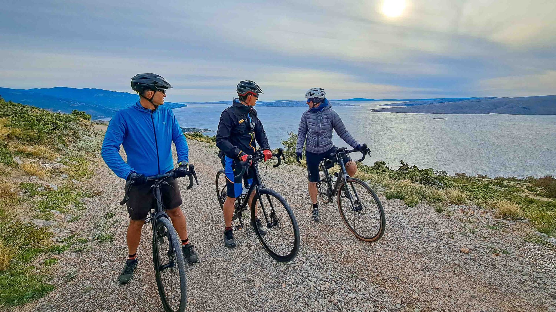 Three people stand on bikes near a lake.