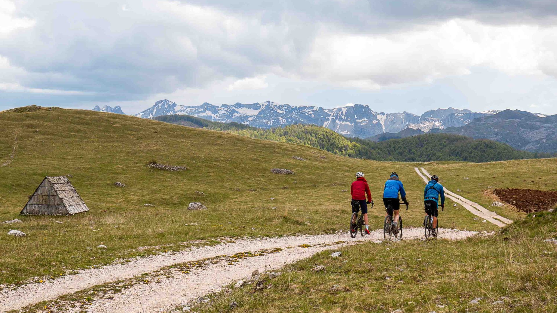 Three cyclists ride a dirt path in the direction of some mountains.