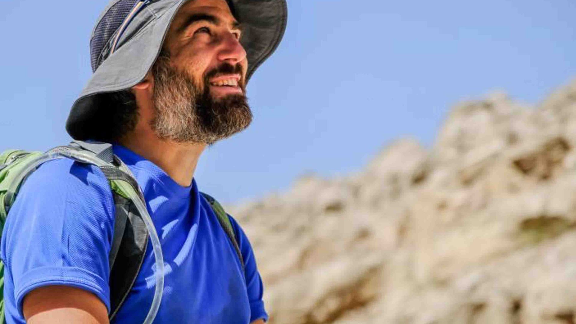 A man in a hat smiles as he looks up toward the sky.