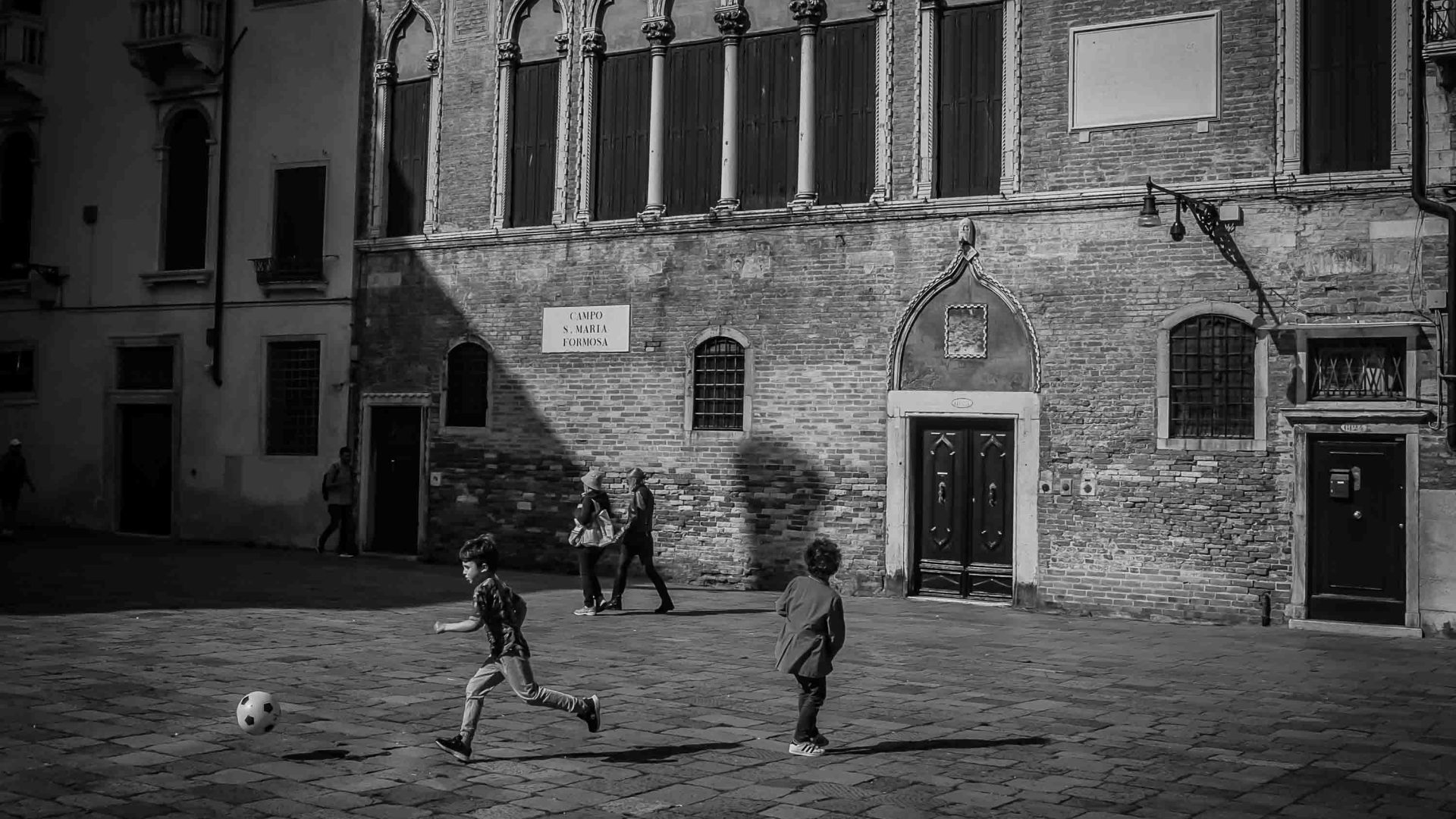 Children play in the street outside a building with arches.