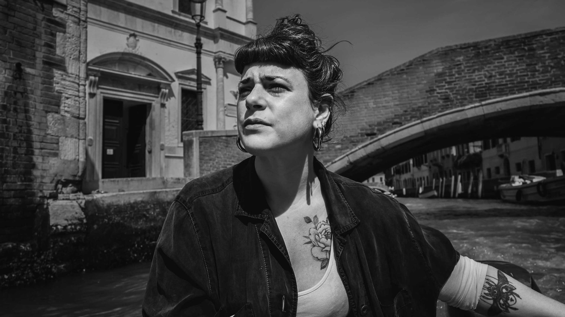 A woman looks off into the distance as she passes by a bridge over a canal.