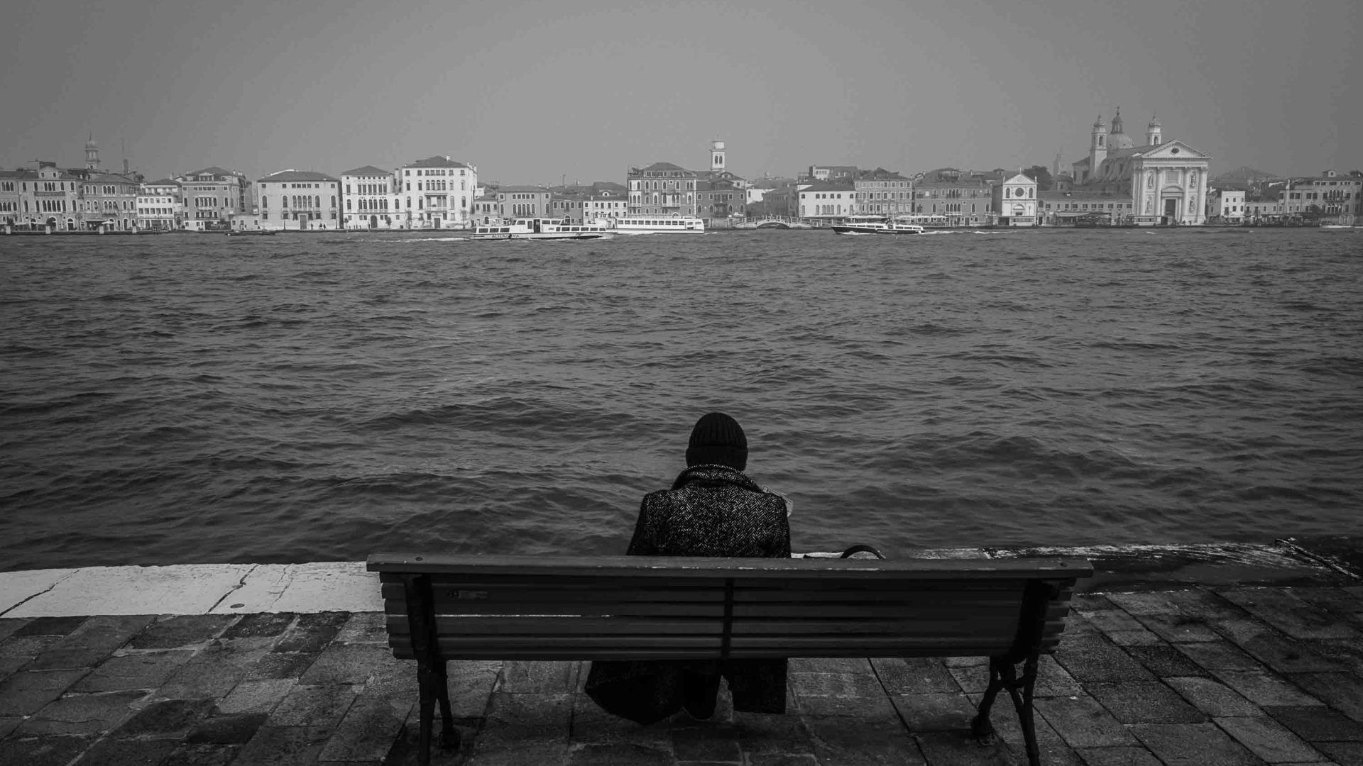 A woman sits on a bench and looks out at the water.