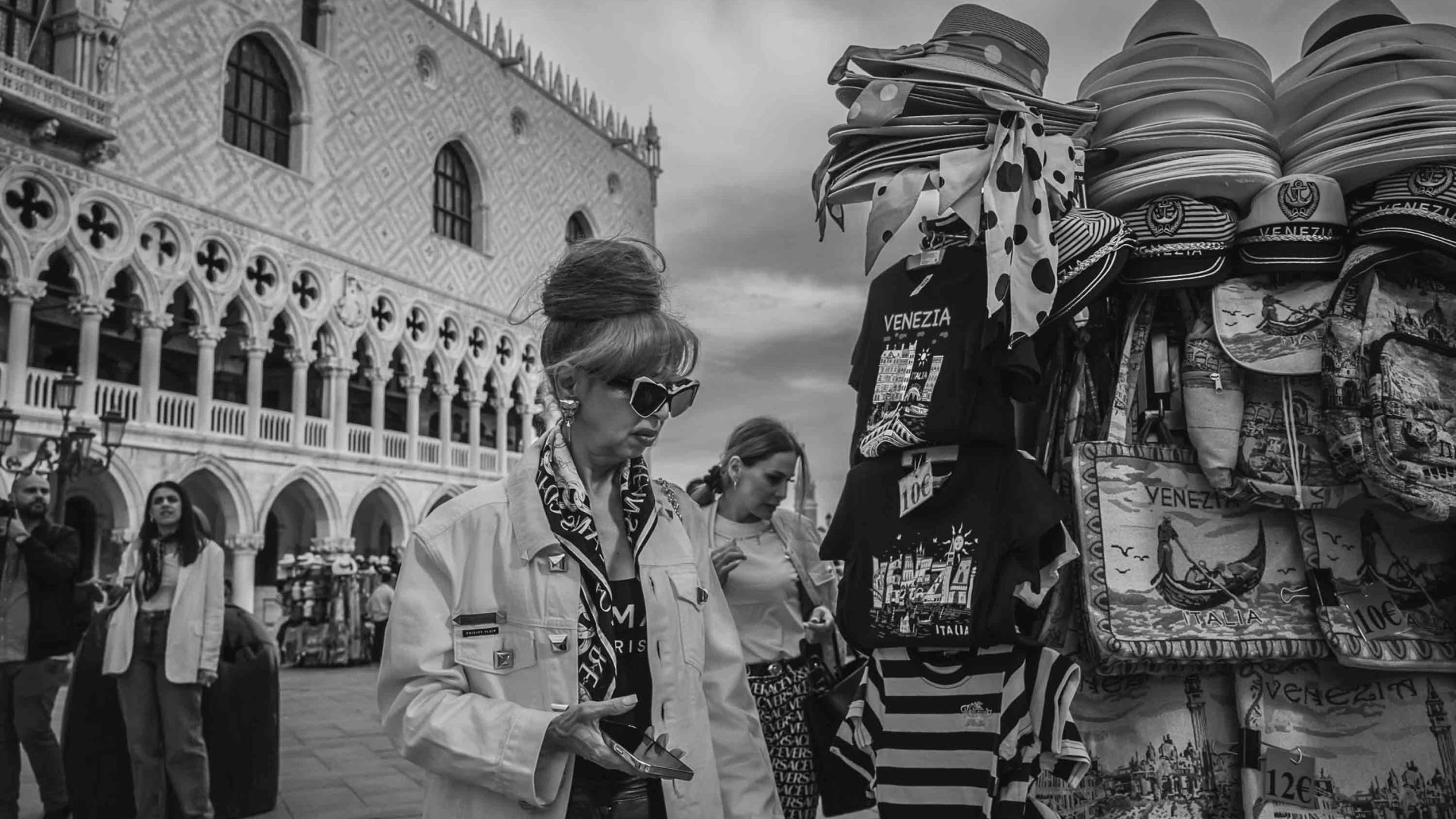 A woman in sunglasses stands alongside a stall selling merchandise in Venice.