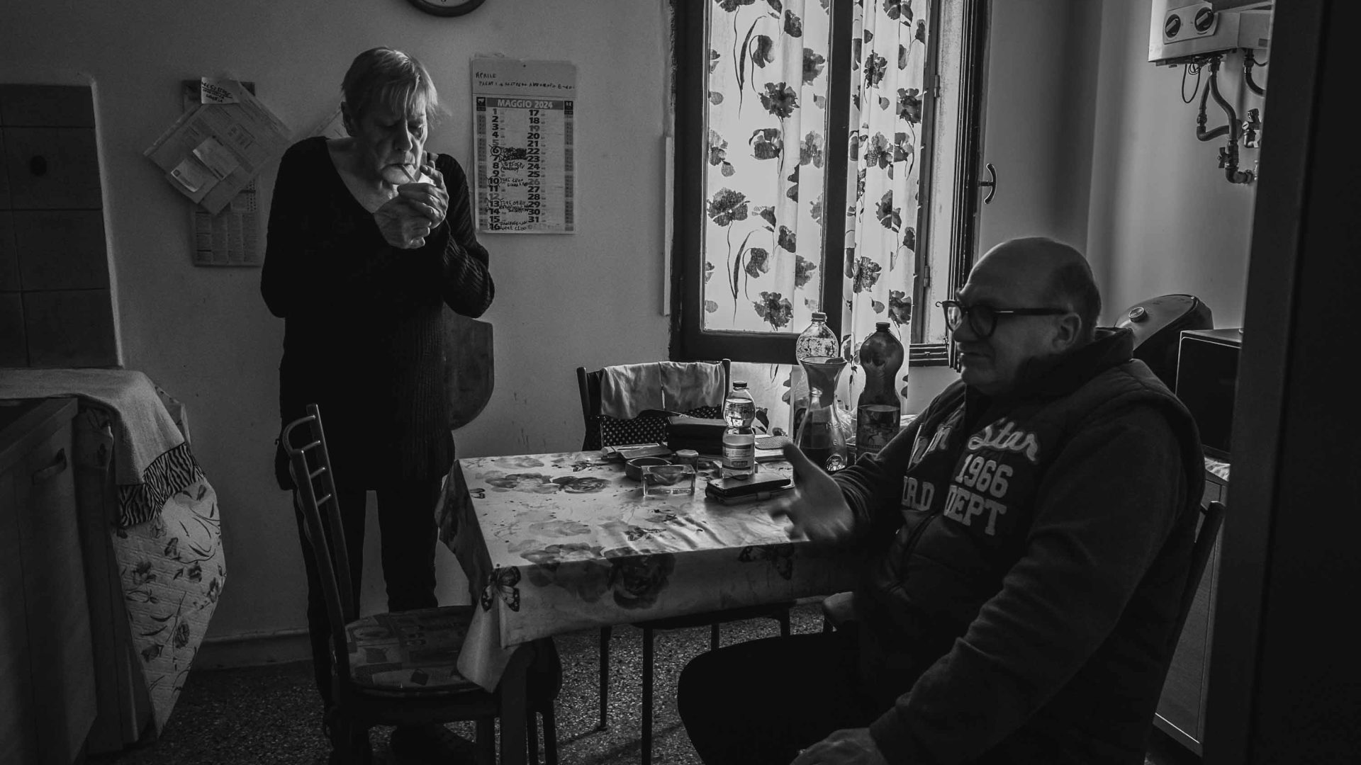 A woman stands next to and a man sits at a table.